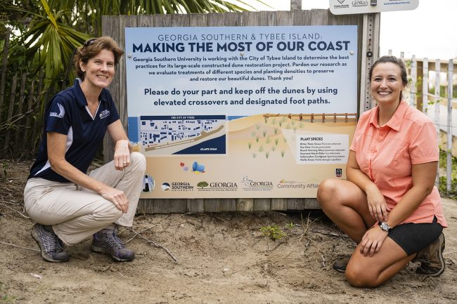 Shannon Matzke, right, poses for a picture with her advisor and Georgia Southern biology professor Lissa Leege, Ph.D., at a sign detailing her sand dune restoration project on Tybee Island.