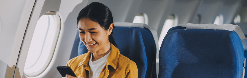 A woman seated in an airplane reading on a mobile phone.