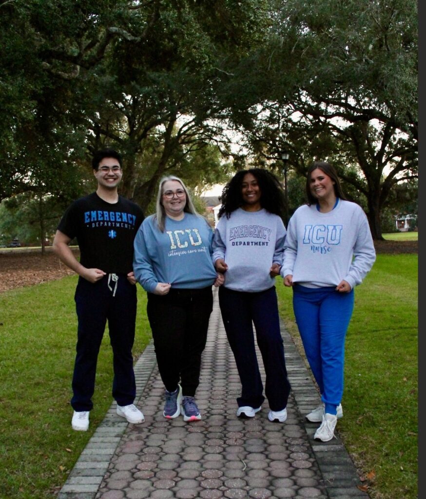 Melissa Miles stands with her classmates. Each of the four individuals is wearing a sweatshirt designating which hospital department they with work in after graduation. Melissa's says "ICU - Intensive Care Unit."
