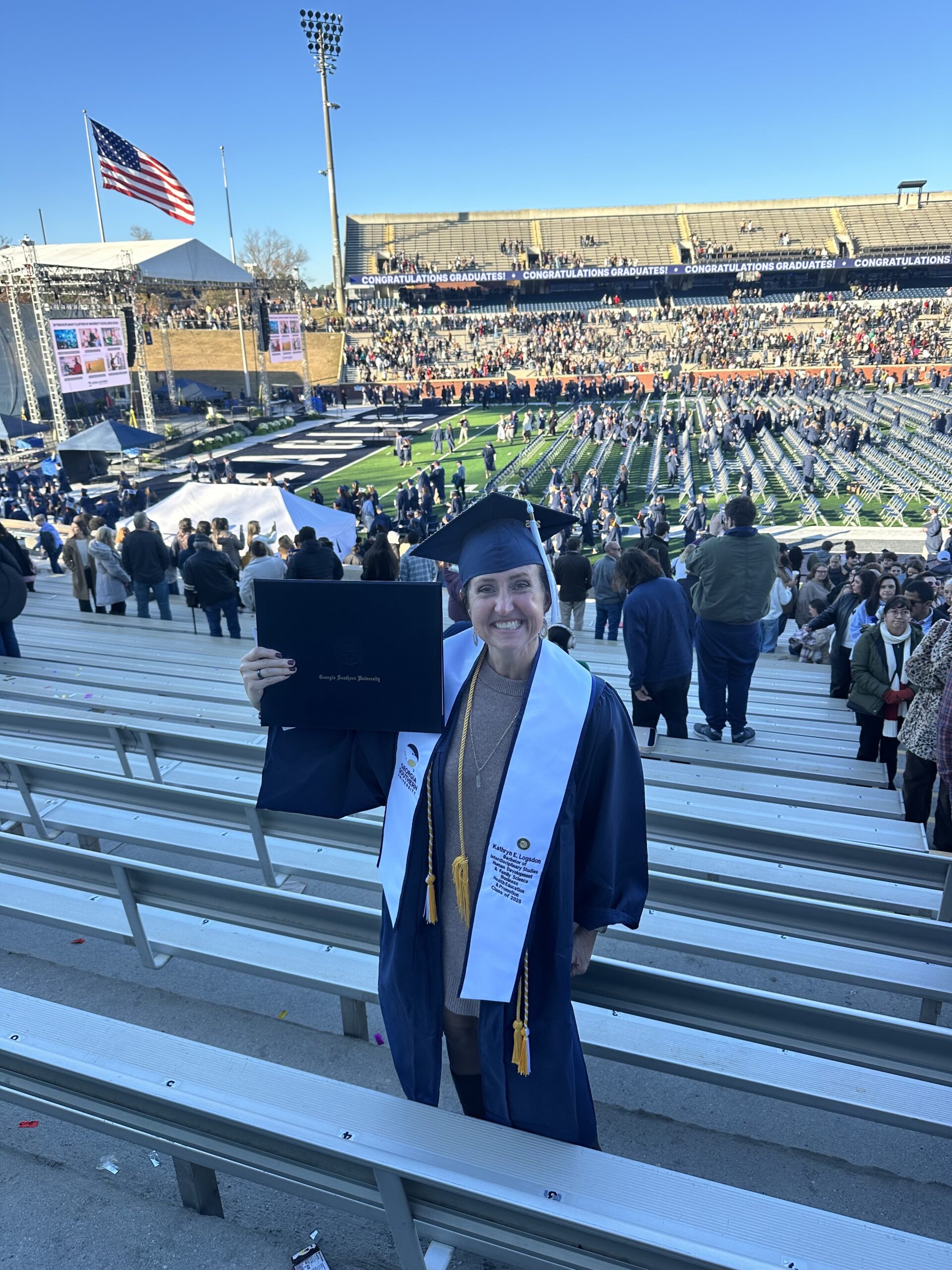 A woman with short brown hair poses with her diploma at Georgia Southern's Paulson Stadium