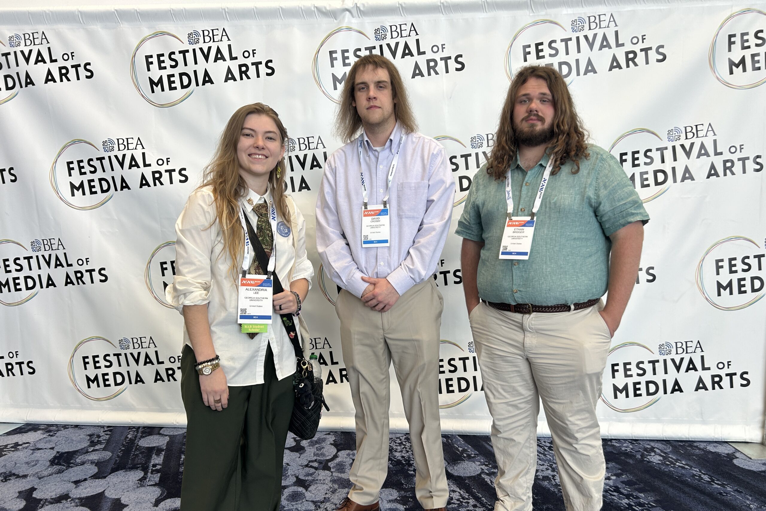 Three students stand in front of a banner that reads "Festival of Media Arts"