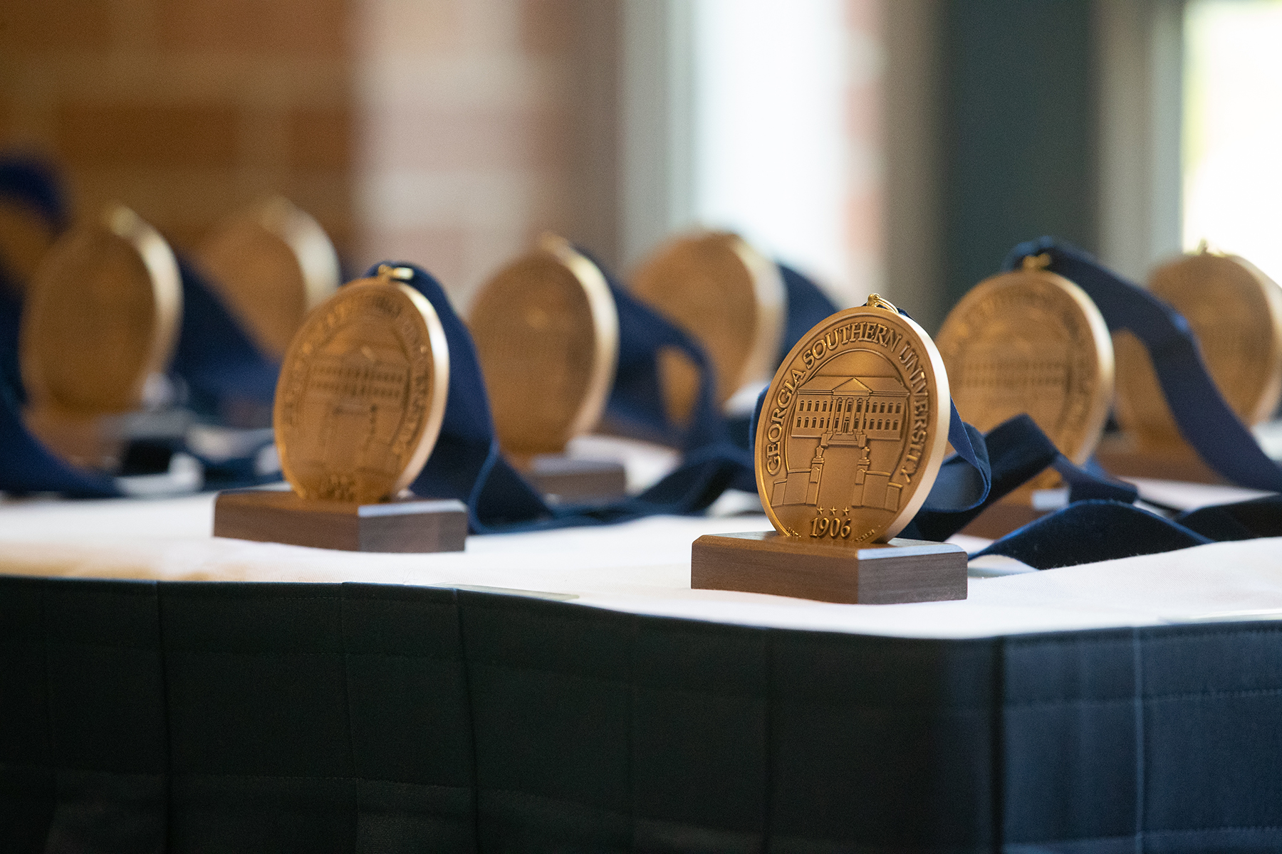Gold medal from Georgia Southern University on a wooden stand with a blue ribbon, displayed on a table.