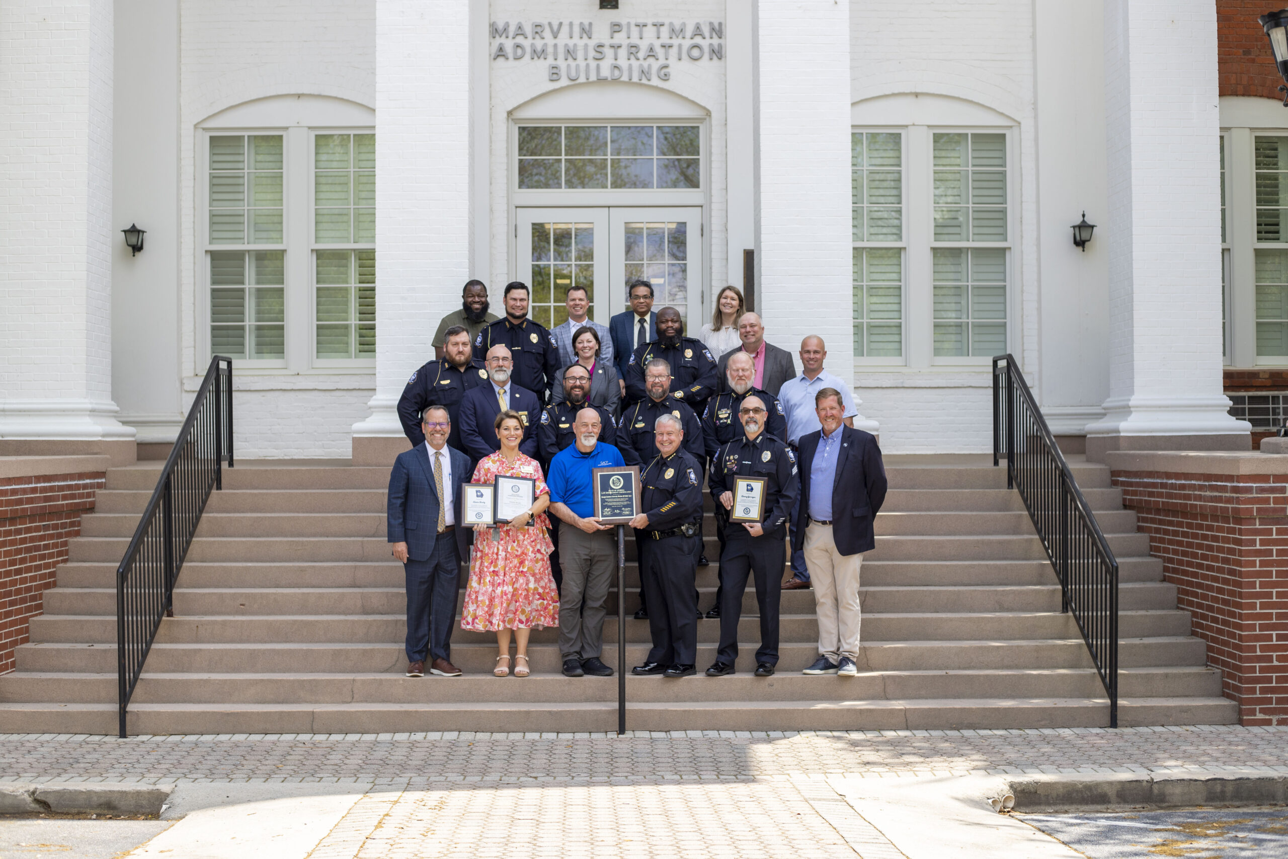 Members of Georgia Southern University leadership and the University Police Department stand on the steps of the Marvin Pittman Administration Building, smiling and holding plaques identifying multiple certifications and awards.