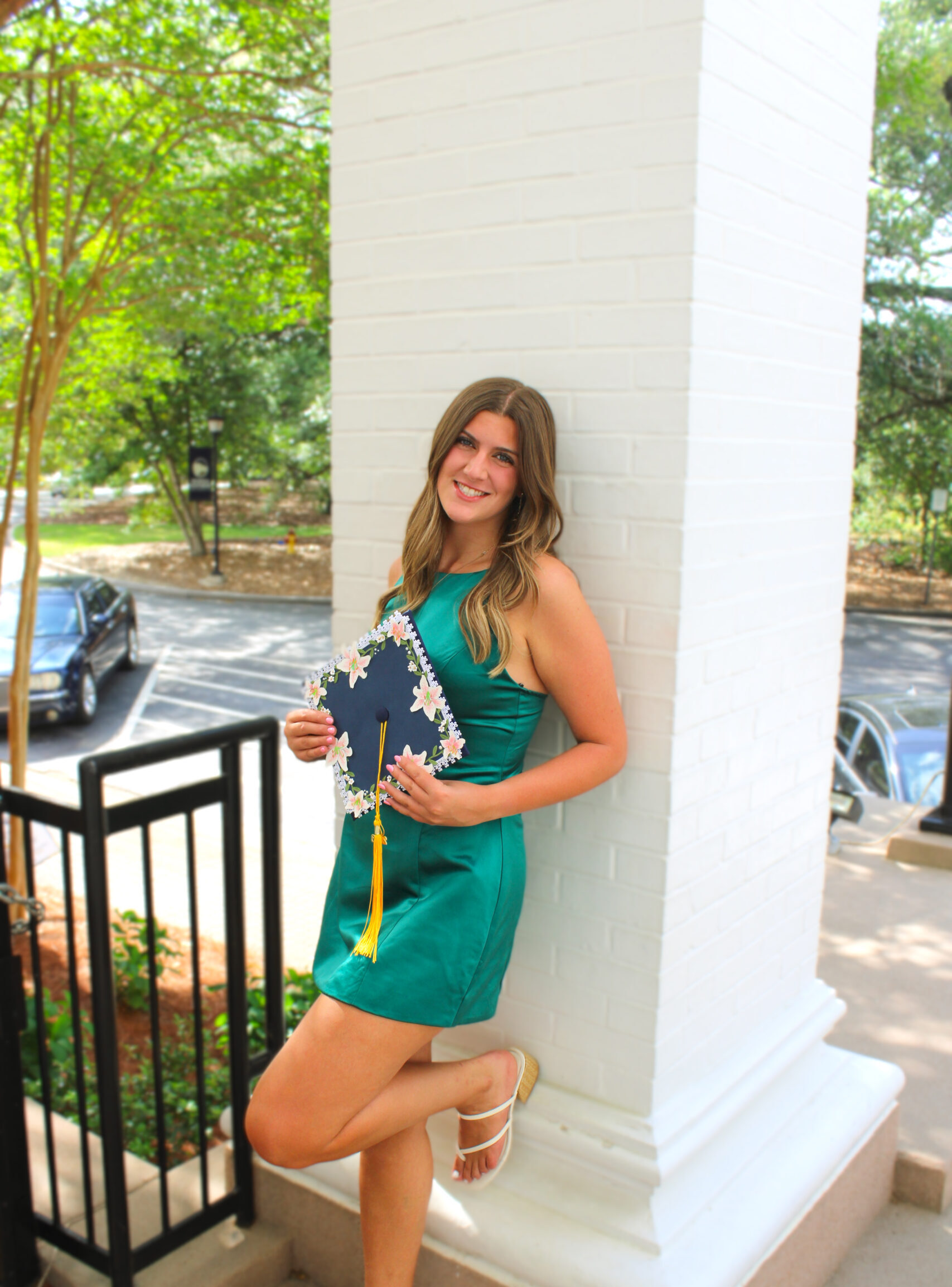 Lily Pavliscsak leans against a white column. She is relaxed and holding her graduation cap.