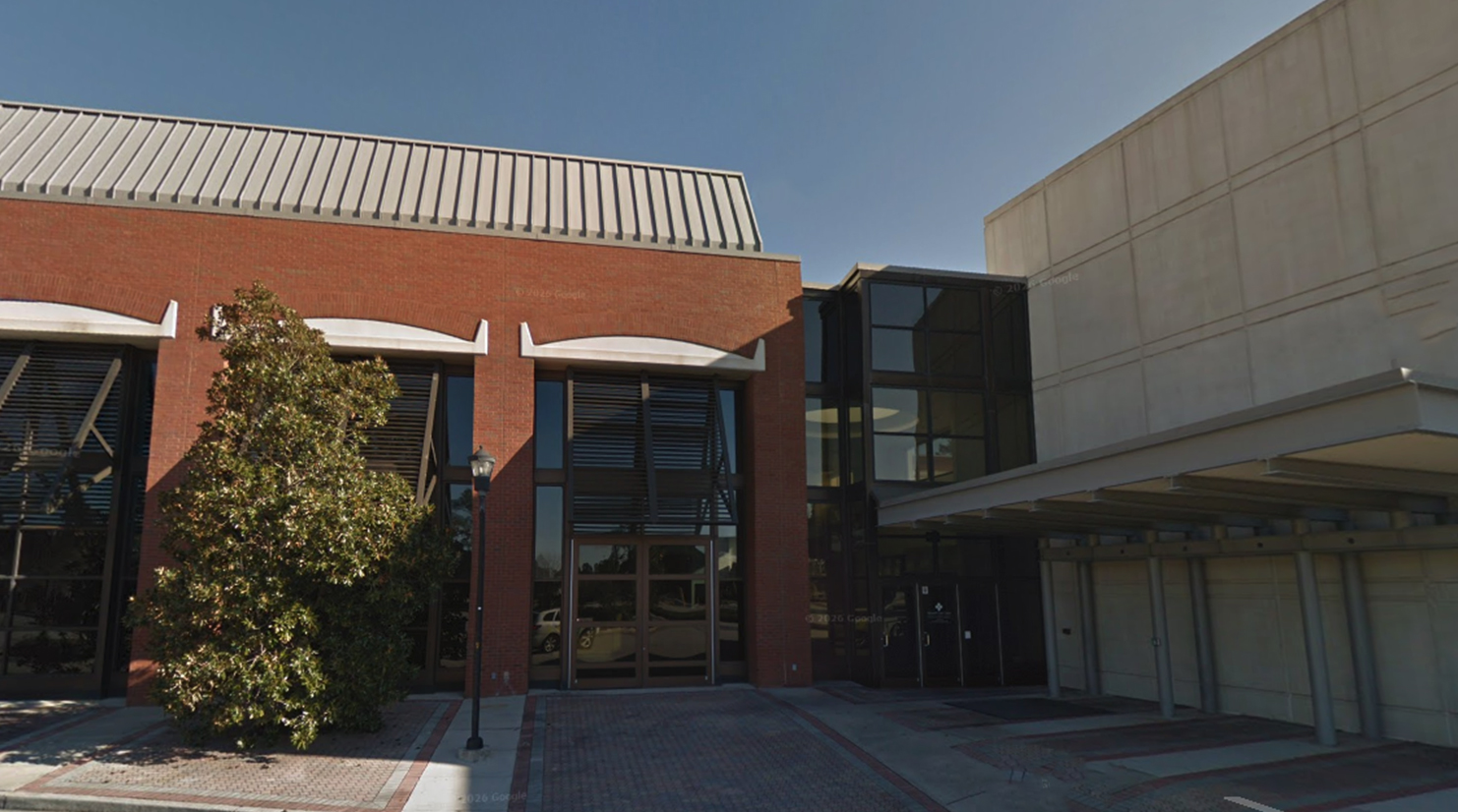 Front view of a brick office building with glass doors, a small tree, and a streetlamp near the entrance.