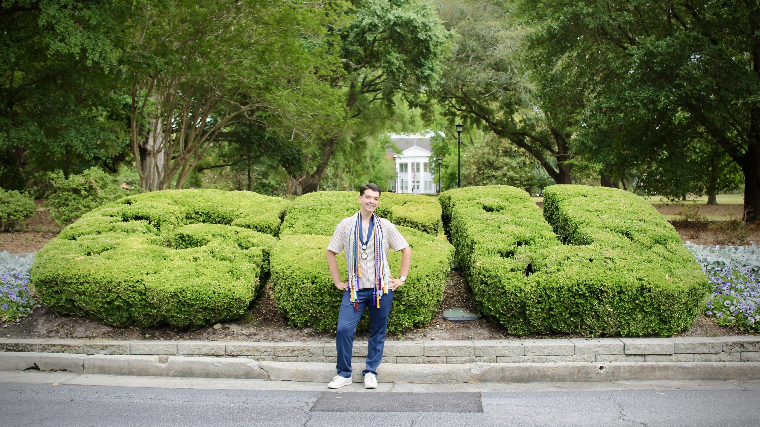 Xander Russell poses in front of the GSU bushes at Georgia Southern University. He is wearing a significant number of honor cords and medallions signifying his various engagements and honors during his time as a student.