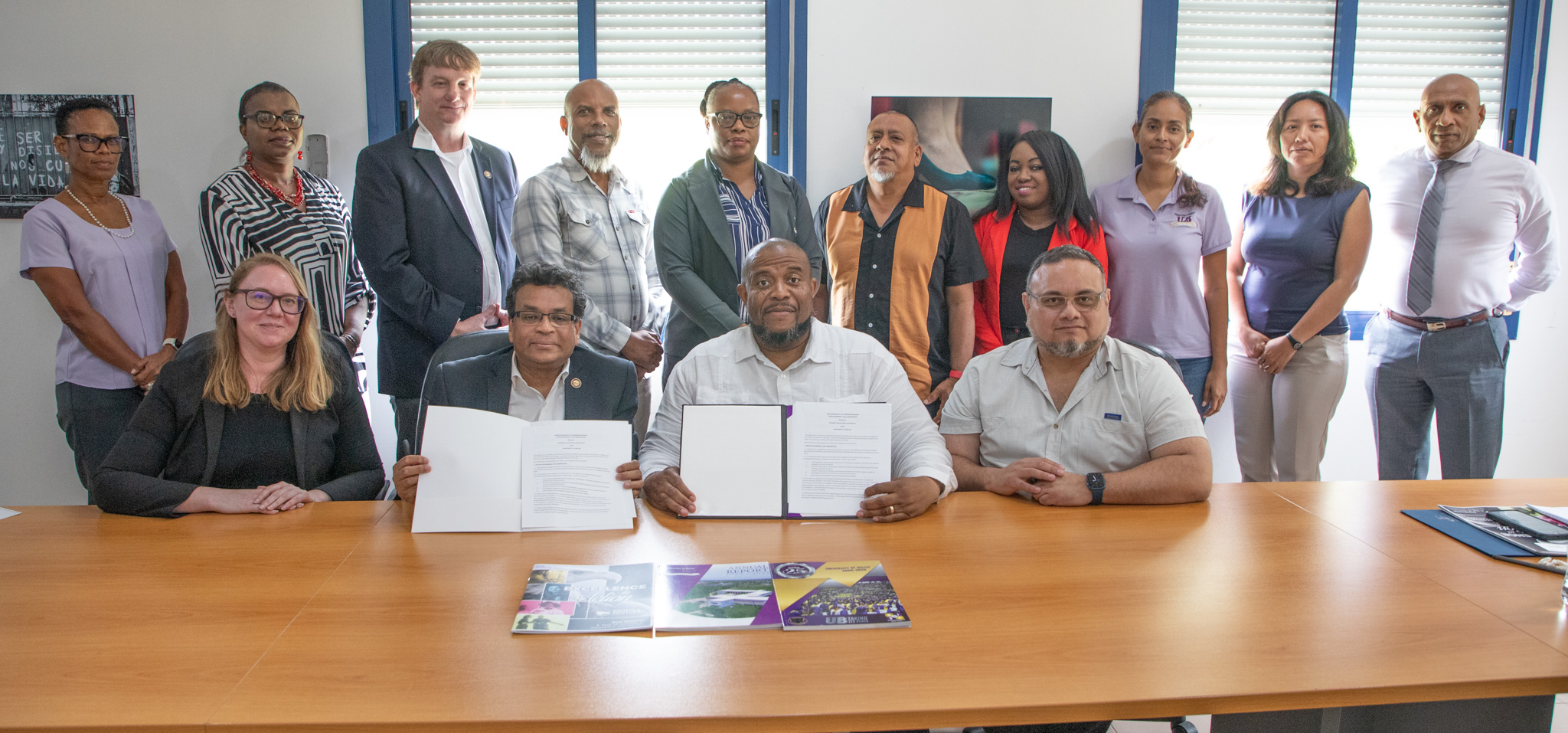 Representatives of Georgia Southern University and the University of Belize pose during a signing ceremony. Two representatives hold documents proudly displaying their signatures.