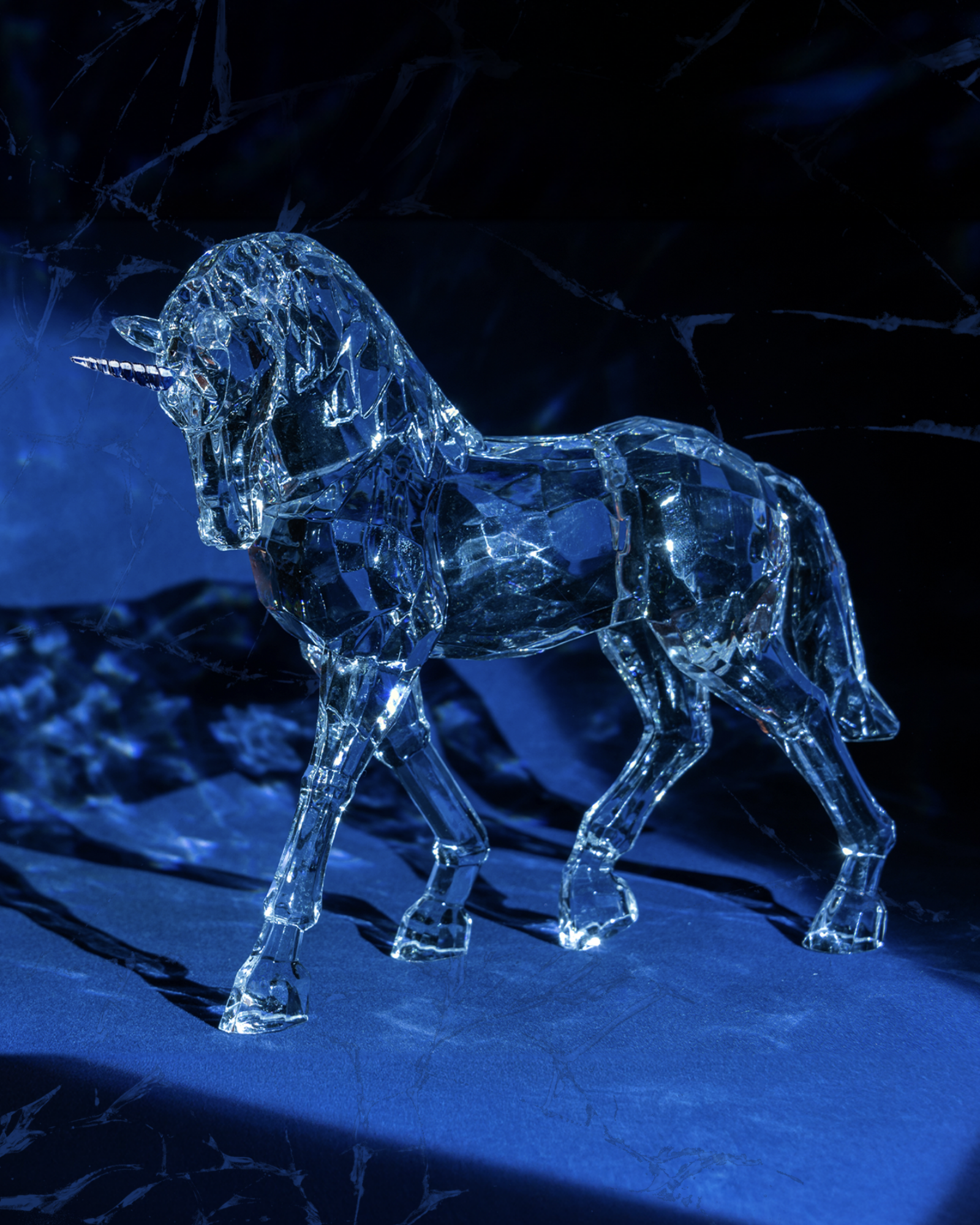Crystal ice-like unicorn sculpture illuminated in blue, standing on a dark surface.