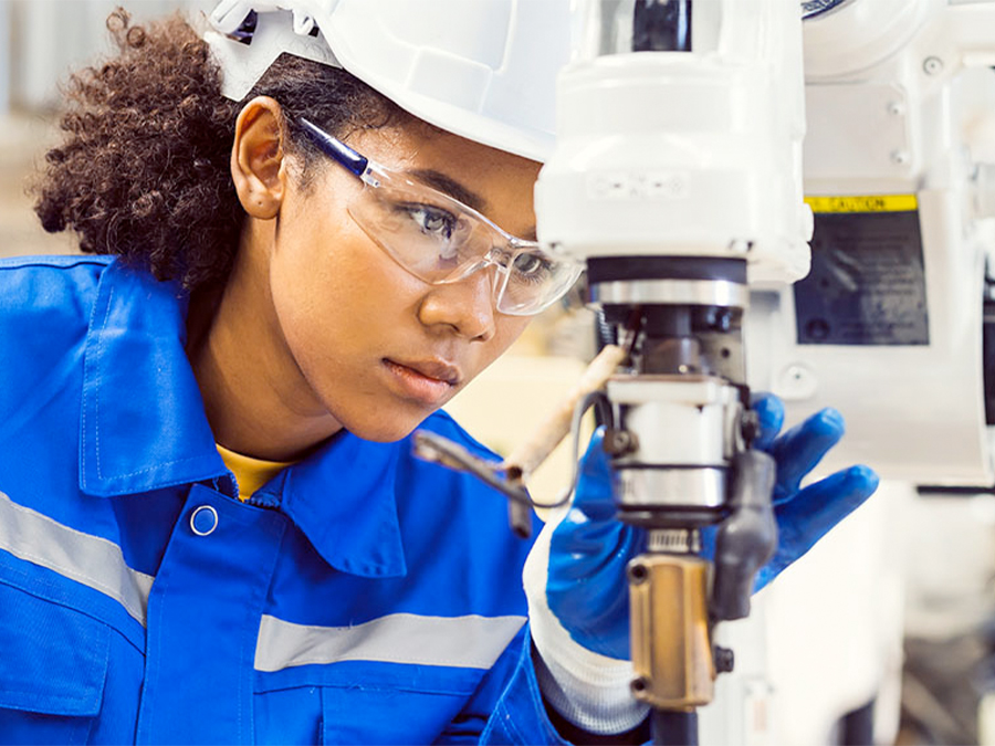 Female technician wearing safety gear inspecting robotic manufacturing equipment.