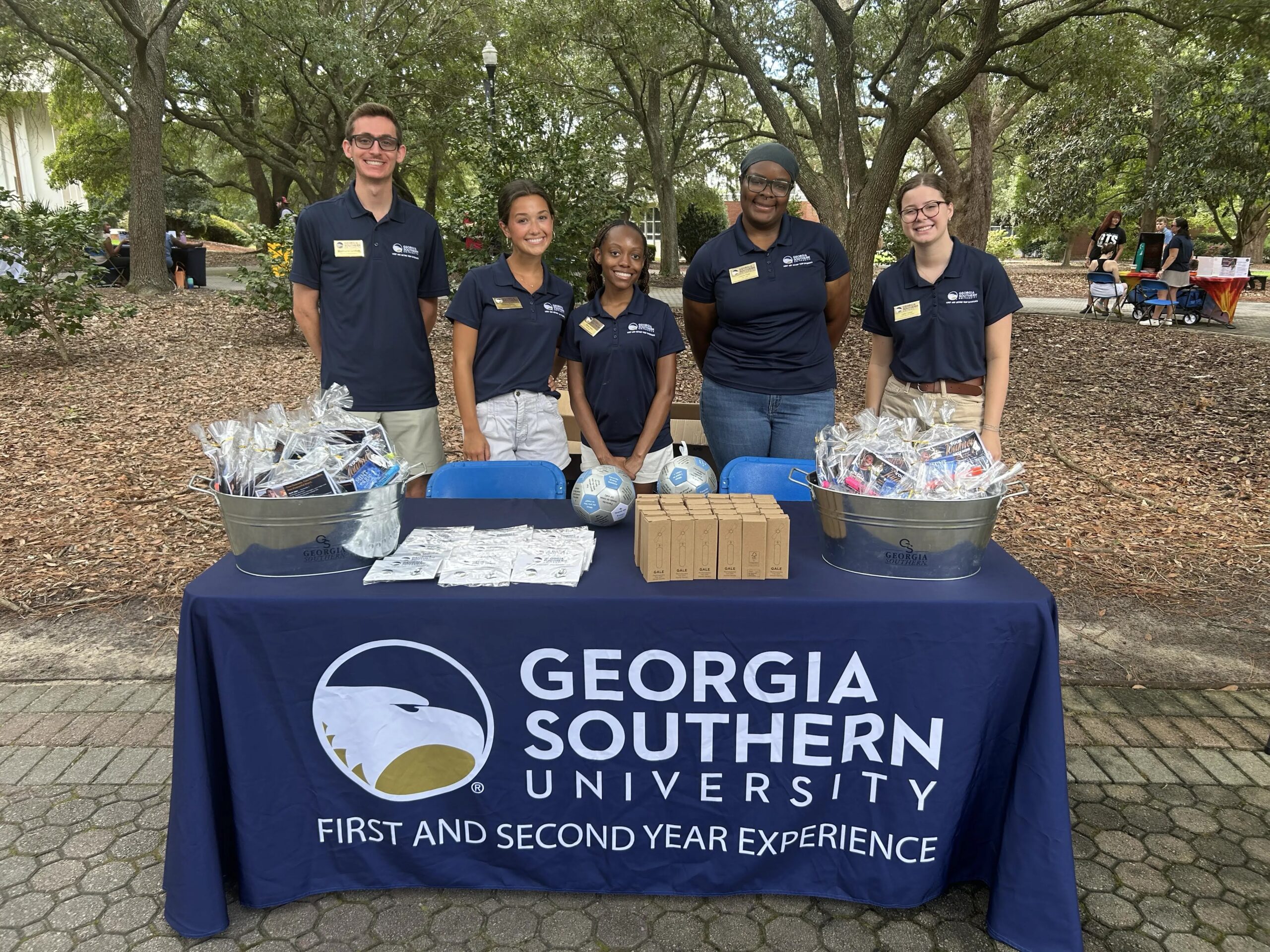 Georgia Southern University Flight Leaders stand behind a table at Boro Browse. The table has a tablecloth featuring the Georgia Southern logo and First and Second Year Experience