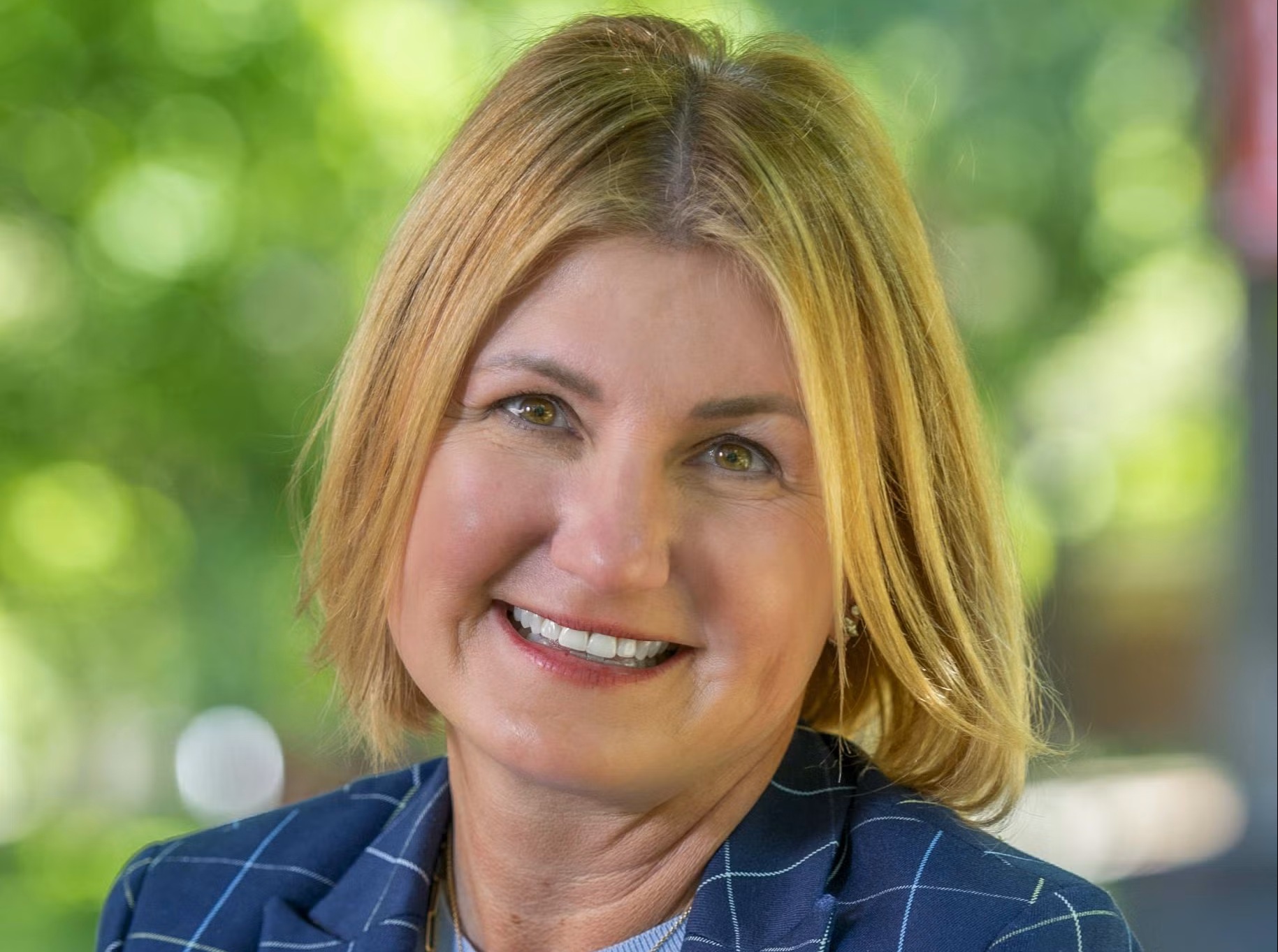 Amy Lingo, Ed.D., dean of the college of education at Georgia Southern University smiles in an outdoor photo. It is a bright, sunny day with light shining through trees in the background.